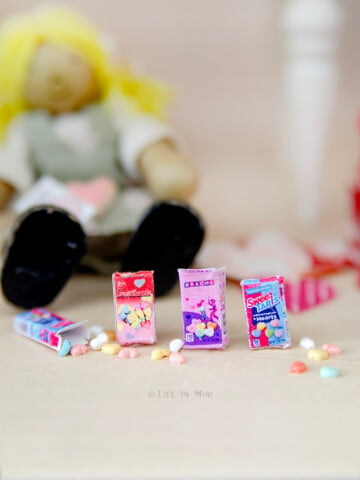 Closeup of 1:12 miniature boxes of candy conversation hearts with tiny colorful heart candies.