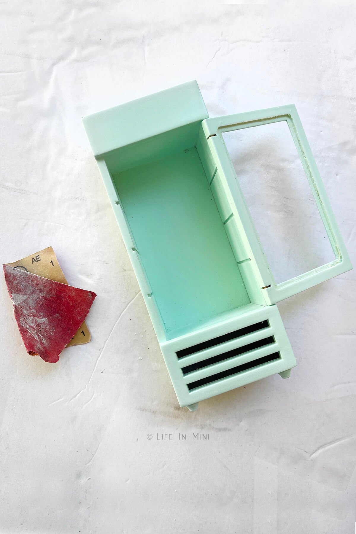 Sanding a green dollhouse refrigerator to paint it.