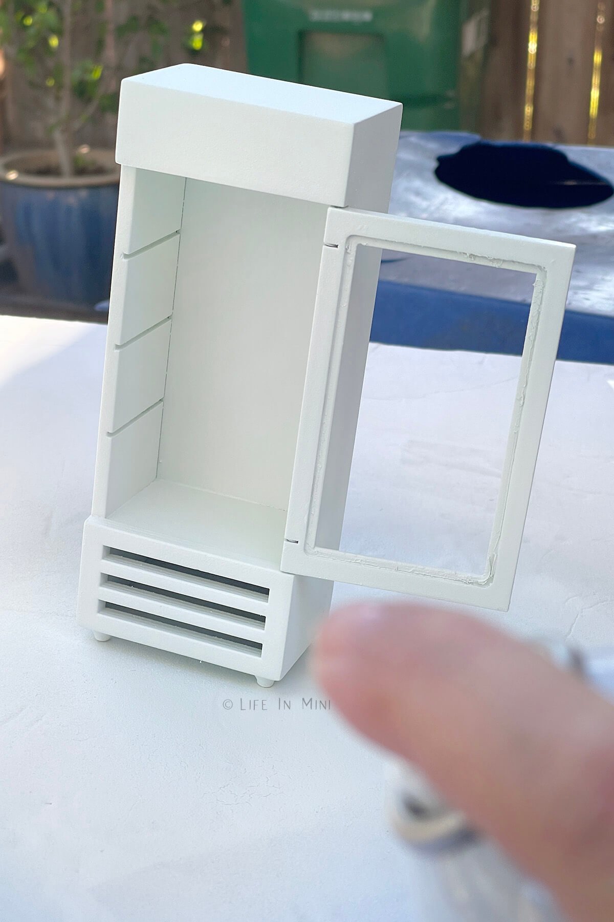 Spray painting a dollhouse refrigerator white.