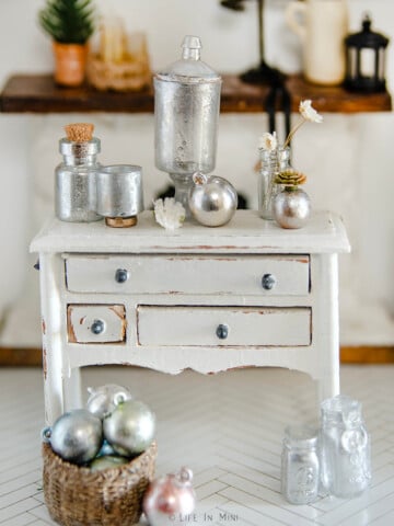 Assorted mercury glass miniatures on a white dresser.