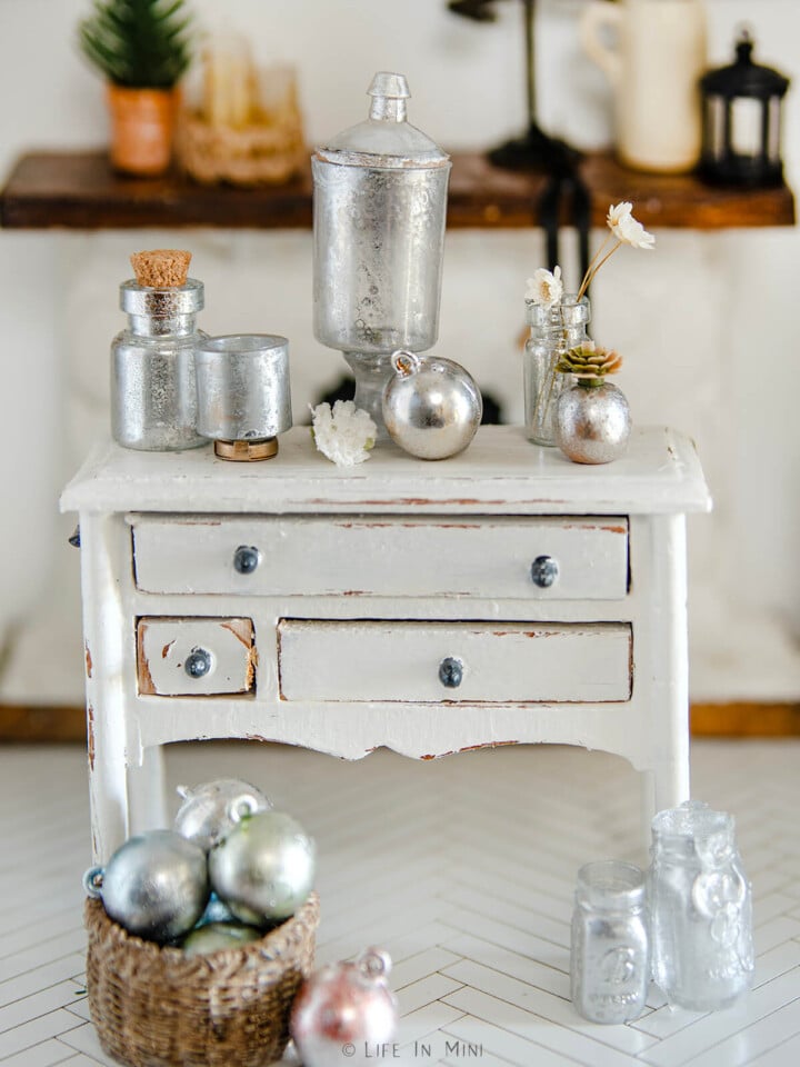 Assorted mercury glass miniatures on a white dresser.