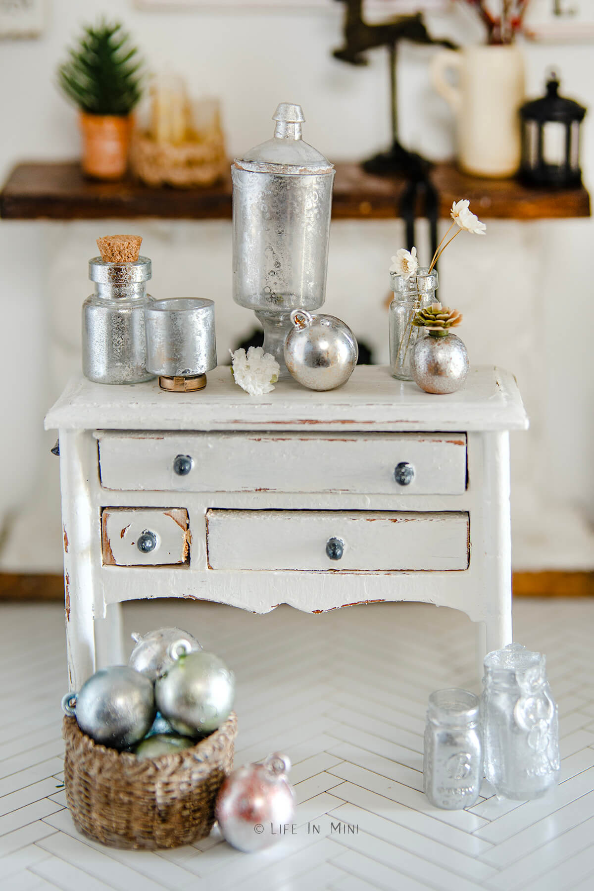 Assorted mercury glass miniatures on a white dresser.