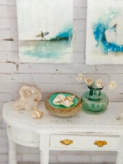 Closeup of assorted mini beach accessories on an antique white dollhouse console table.