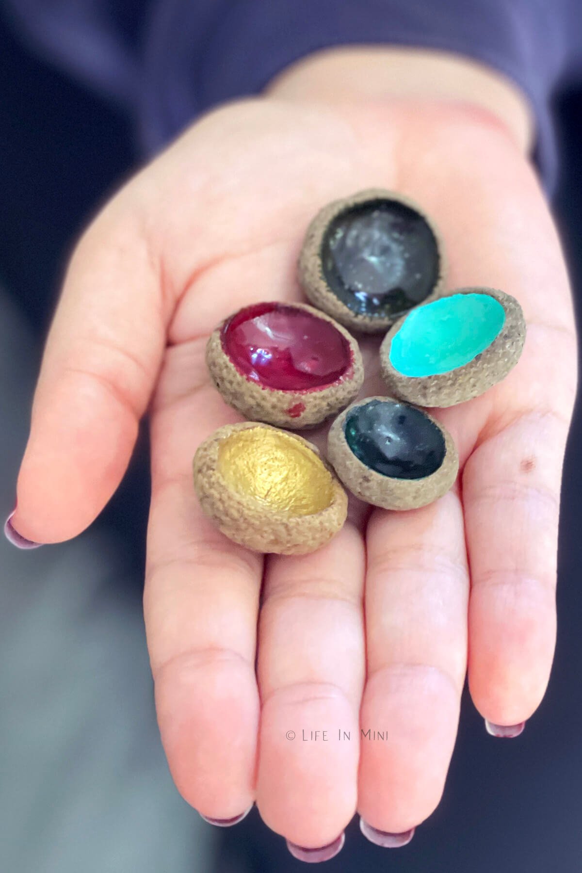 A hand holding several acorn caps painted different colors.