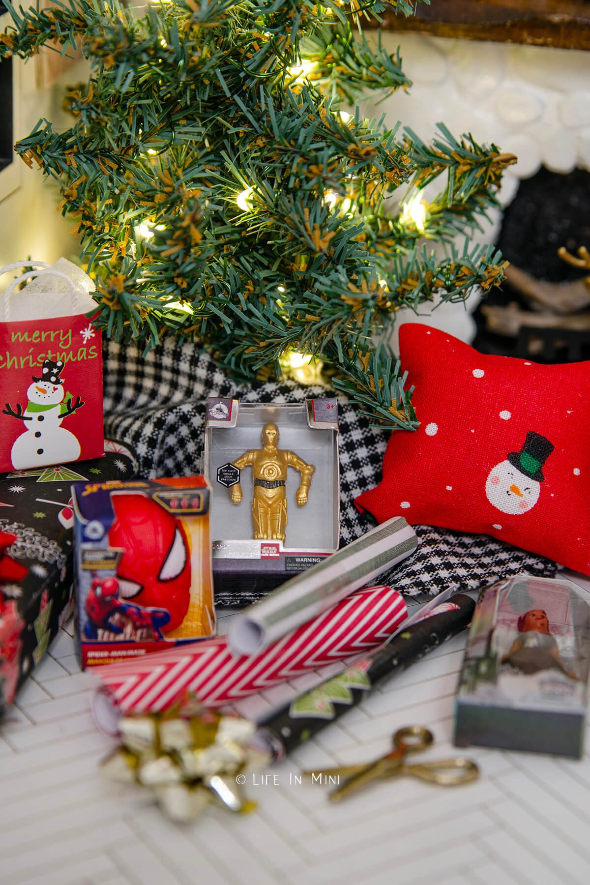 Closeup of miniature toys, wrapping paper and gifts next to a dollhouse Christmas tree.