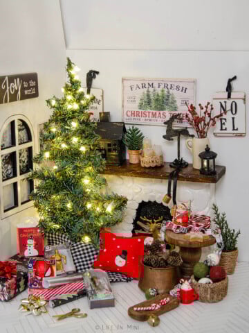 A dollhouse living room decorated for Christmas including a lit tree, presents and lots of other Christmas decorations.