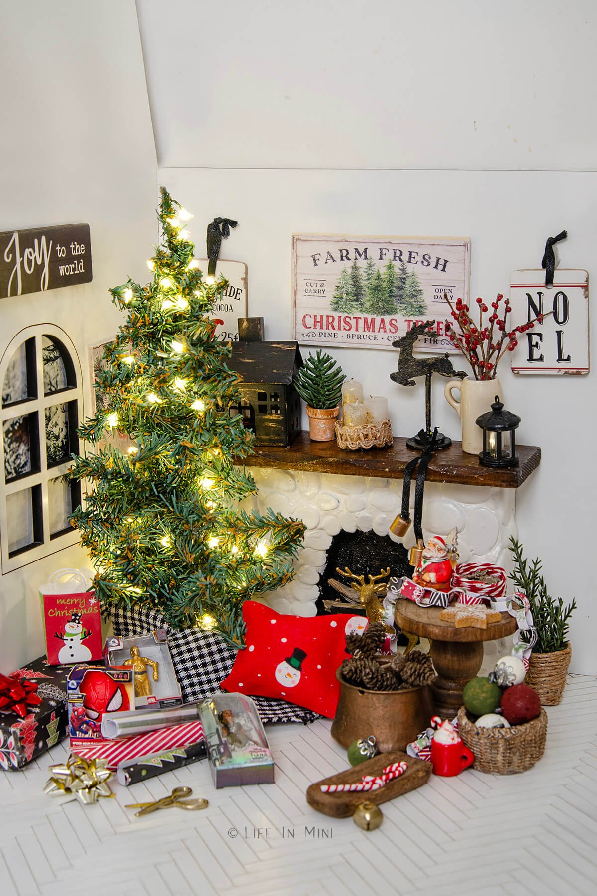 A dollhouse living room decorated for Christmas including a lit tree, presents and lots of other Christmas decorations.
