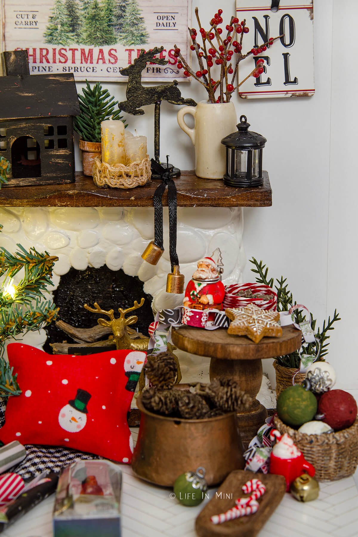 A dollhouse scene showing a small table in front of a fireplace with a miniature Santa beer stein and other Christmas decorations.