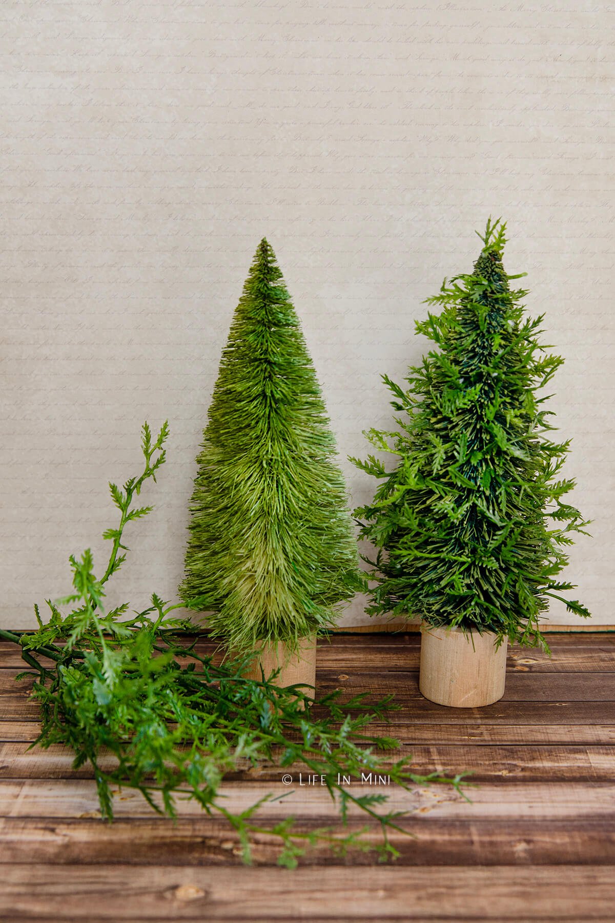Two bottle brush Christmas trees where one is spruced up with added greenery.
