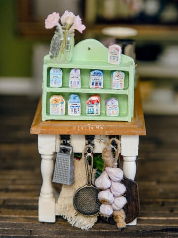 A green spice rack with miniature spice village in it sitting on a kitchen table in a dollhouse.